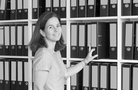 Melanie Scheibel im BĂĽro an einem Regal mit Aktenordnern